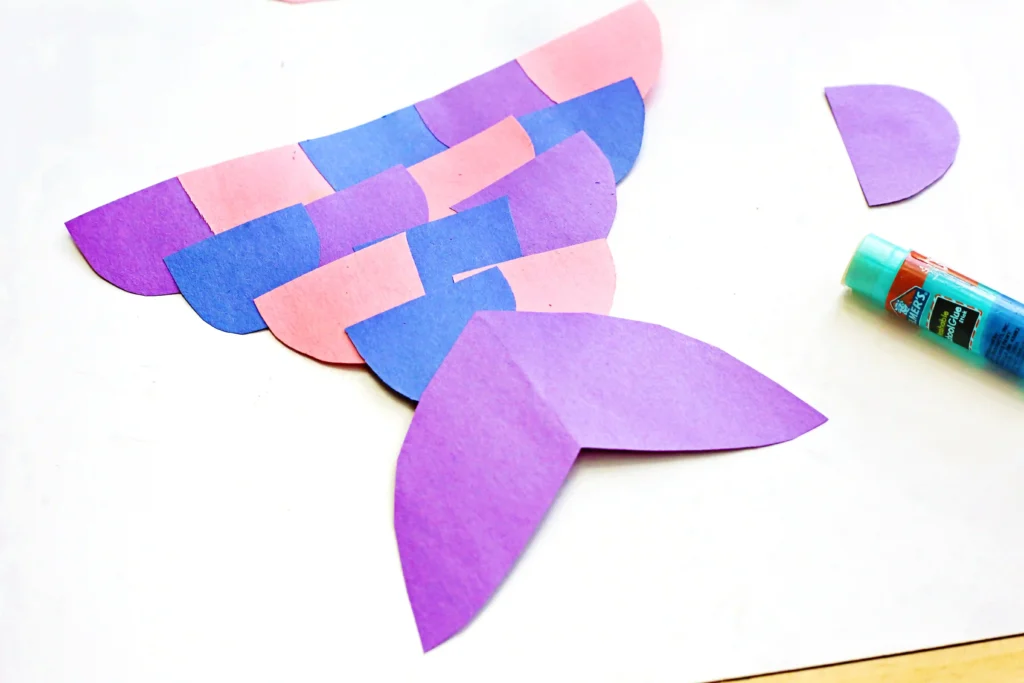 Colorful paper shapes (pink and purple half circles) arranged on white background, with a glue stick nearby