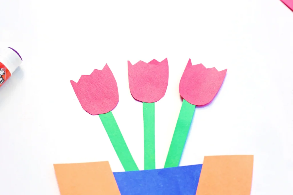 Colorful paper tulips with pink petals and green stems in an orange-blue pot on a white background
