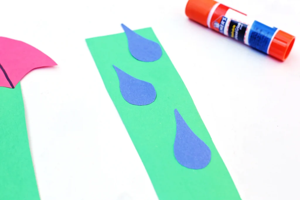 an umbrella craft that has a green U cut out of construction paper with blue raindrops glued on