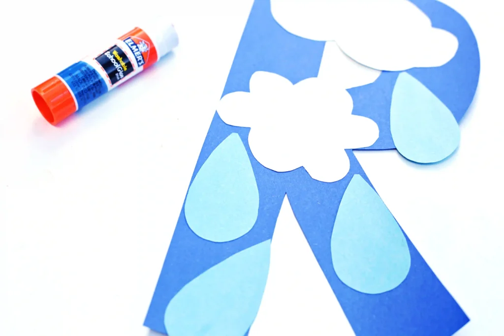 rain craft for kids that has a letter R cut out of blue construction paper with rain drops and clouds