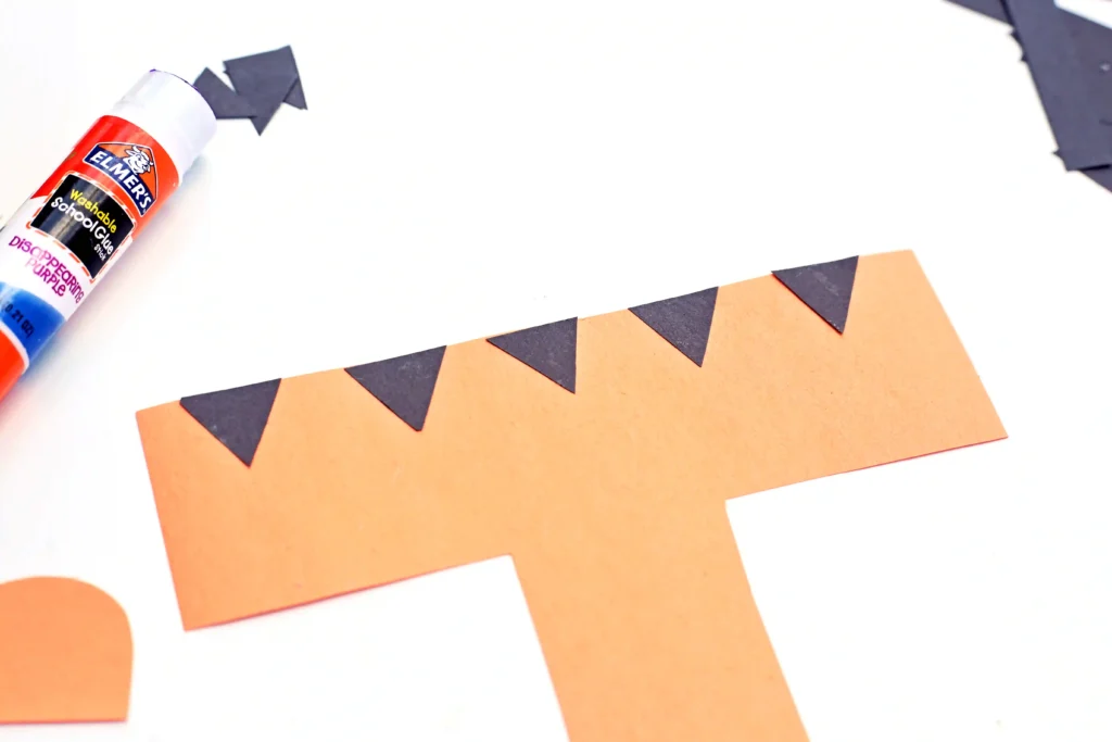 an alphabet craft with a letter t cut out of orange construction paper with black triangles glues on top