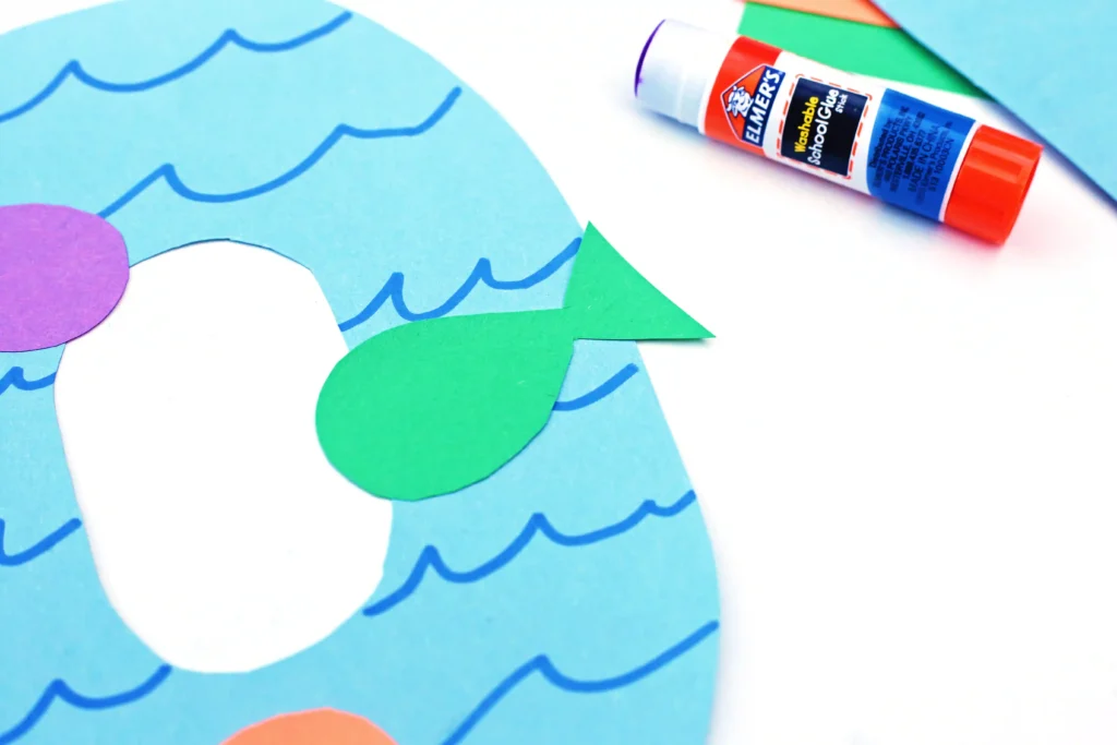 an ocean themed craft that is a letter o cut out of blue construction paper with wavy lines drawn on and a green construction paper fish glued on top