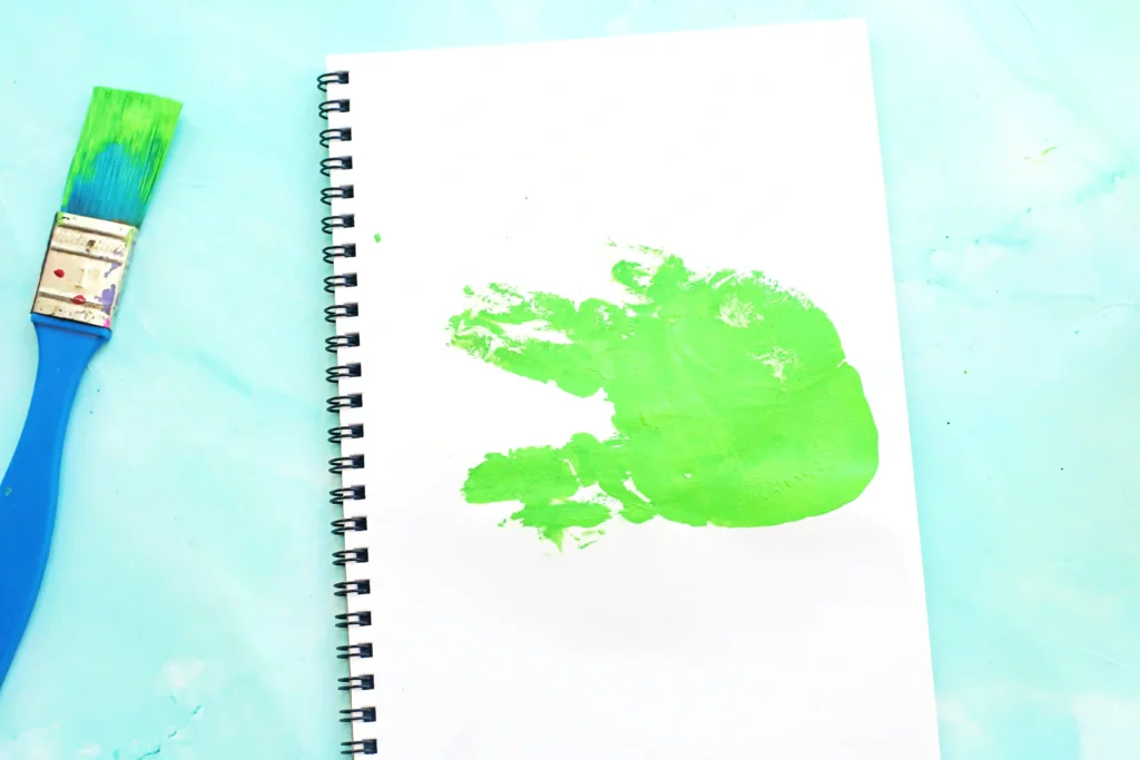 a green handprint on a piece of paper with a paintbrush on the side for this alligator craft