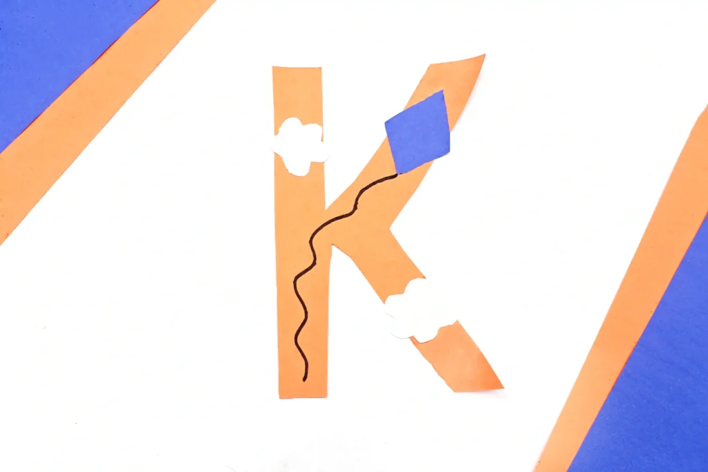 a letter k craft cut out of construction paper with a kite and clouds