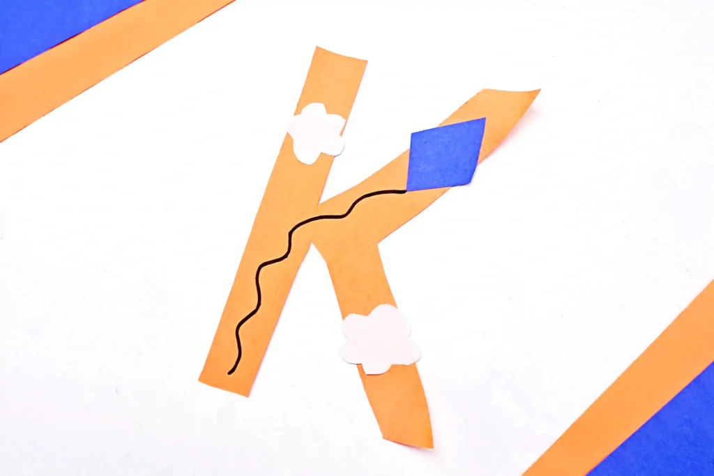 a letter k cut out of construction paper with a kite and clouds