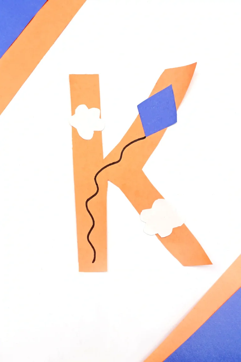 a letter k cut out of construction paper with a kite and clouds