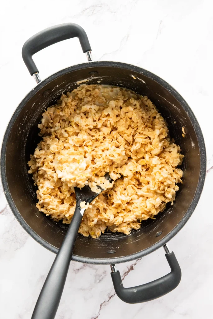 Top-down view of a black pot filled with rice cereal and a spoon resting inside it on a light surface.
