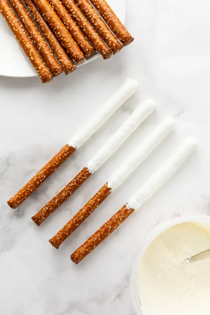 white chocolate coated pretzel rods arranged on a white plate, some with white chocolate at the ends.