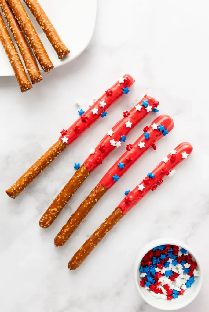 Pretzel sticks coated in red icing with white and blue star sprinkles on a white surface.