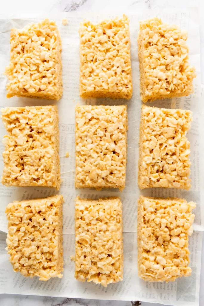 Grid of square puffed-rice cereal bars with a caramel color on parchment paper