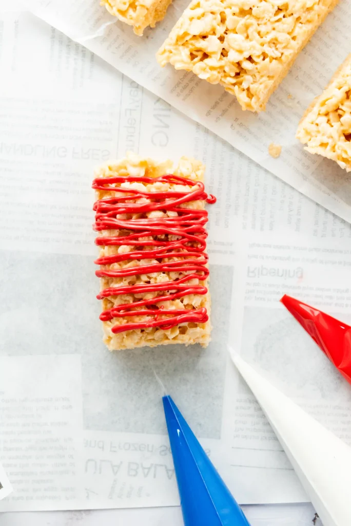 Rice Krispies treat drizzled with bright red icing on parchment paper.