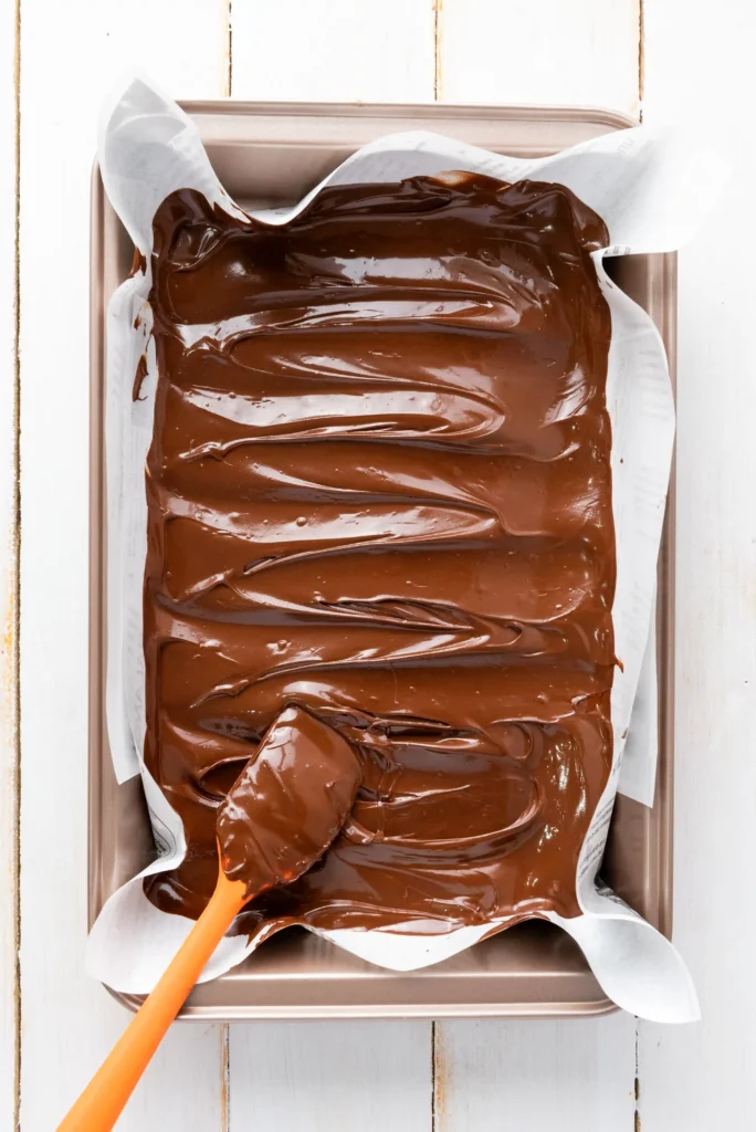 Loaf pan lined with parchment paper, filled with glossy melted chocolate batter and an orange spatula resting in the mixture for this memorial day dessert