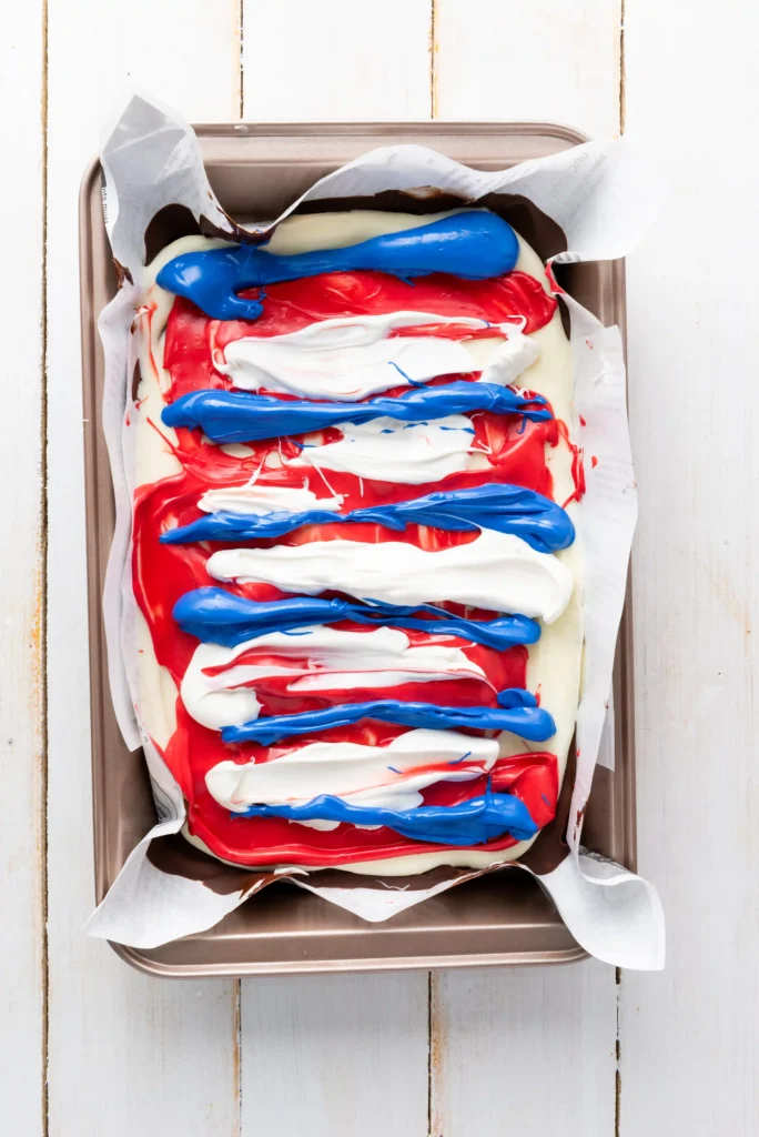 Rectangular chocolate bark in a metal pan, swirled with red, white, and blue frosting on parchment.