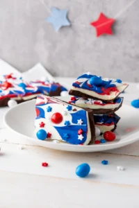 a red, white and blue patriotic dessert -chocolate bark with patriotic m&ms on a white plate