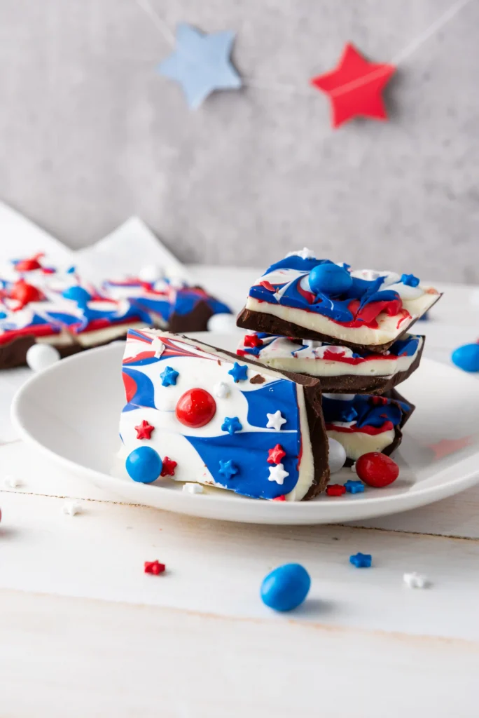a red, white and blue patriotic dessert -chocolate bark with patriotic m&ms on a white plate