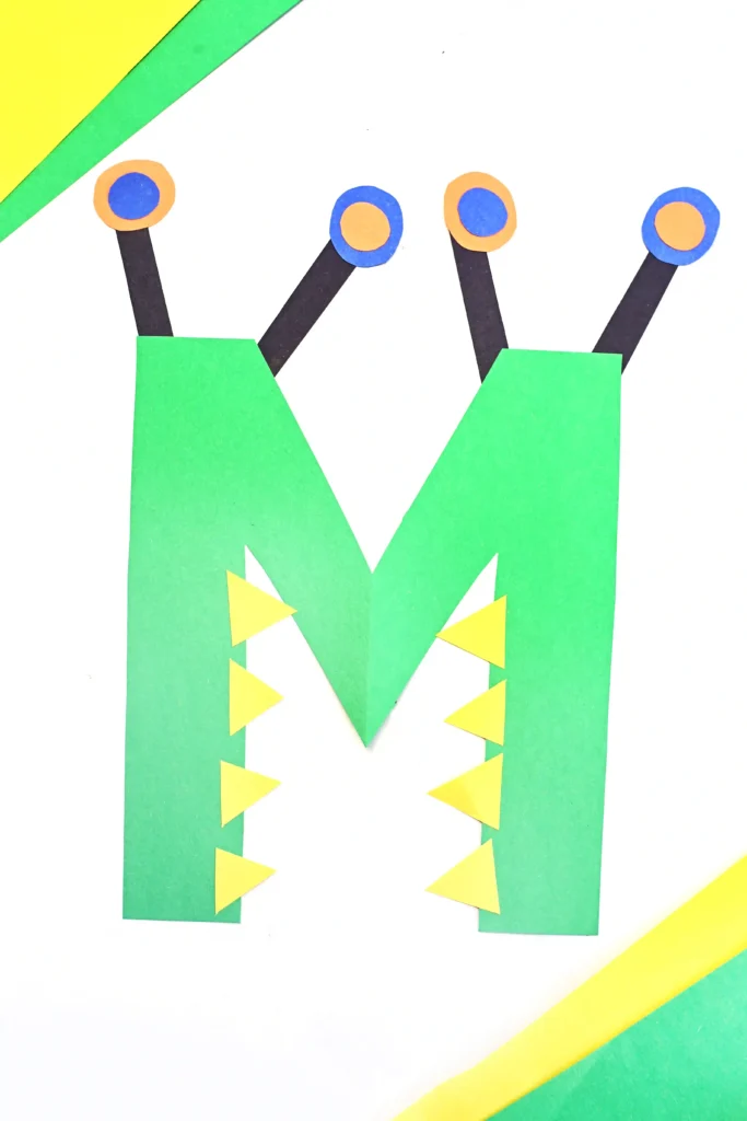 a letter activity for kids made out of construction paper with a green letter m that has eyes and teeth