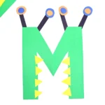 a letter m monster craft made out of construction paper with a green letter m that has eyes and teeth