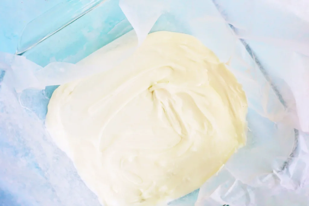 Close-up of a mound of melted white chocolate on crinkled parchment paper with a light blue background.