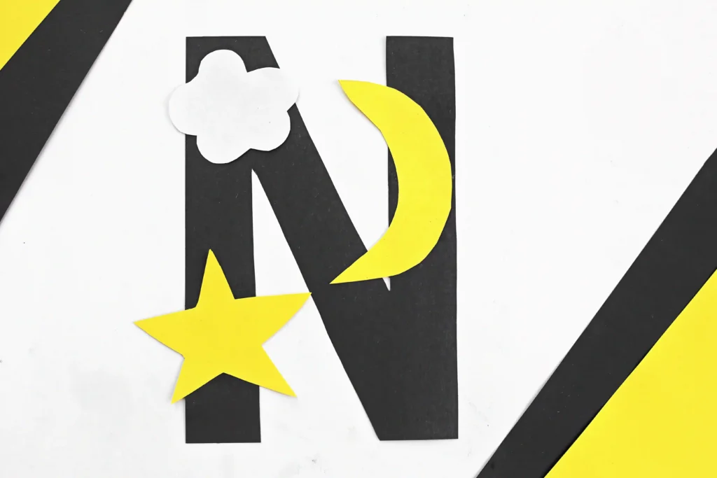 a letter n cut out of black construction paper with a yellow star, yellow moon, and white cloud glued on