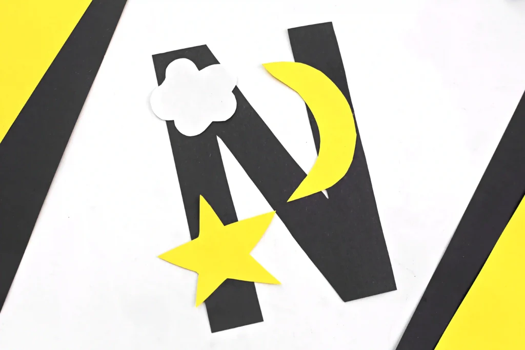 a letter n cut out of black construction paper with a yellow star, yellow moon, and white cloud glued on