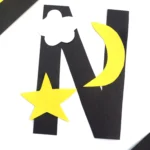 a letter n cut out of black construction paper with a yellow star, yellow moon, and white cloud glued on