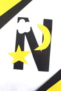 a letter n cut out of black construction paper with a yellow star, yellow moon, and white cloud glued on
