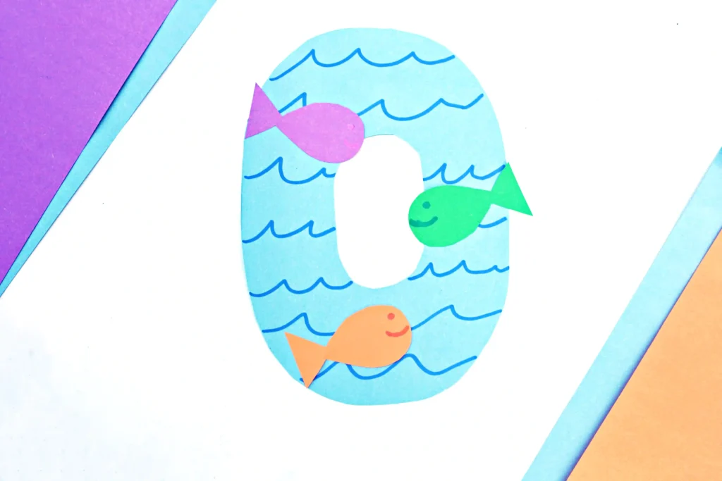a letter O cut out of blue paper with blue waves drawn on and colorful paper fish glued on top to make a letter craft for preschoolers
