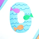 a letter O cut out of blue paper with blue waves drawn on and colorful paper fish glued on top to make a letter craft for preschoolers