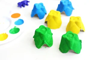 Bright green, blue, and yellow clay pieces on a white surface with a paint palette edge visible in the background.