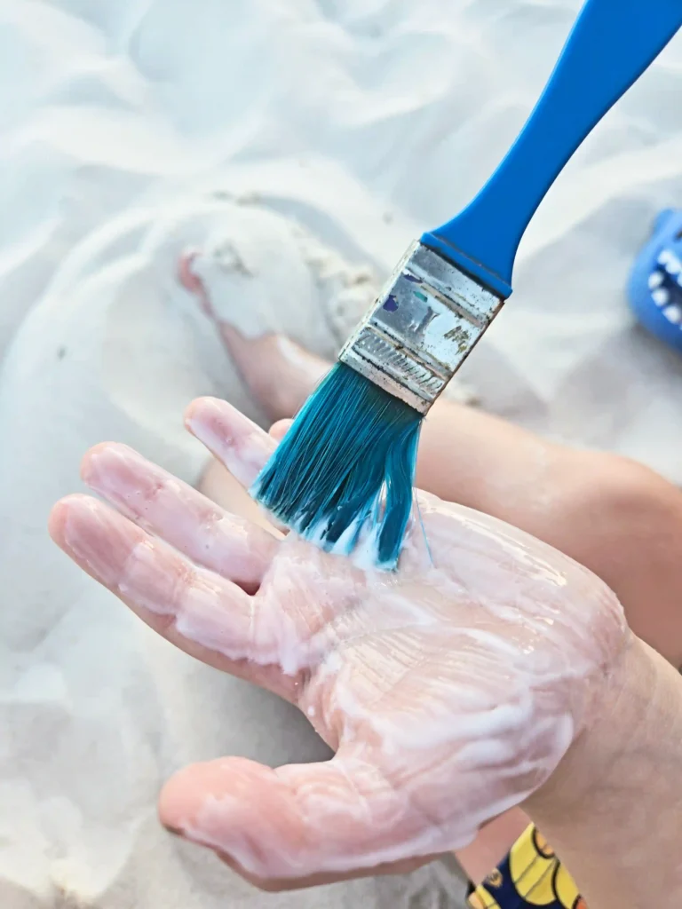 Close-up of a blue paintbrush applying glue onto a kid's hand.