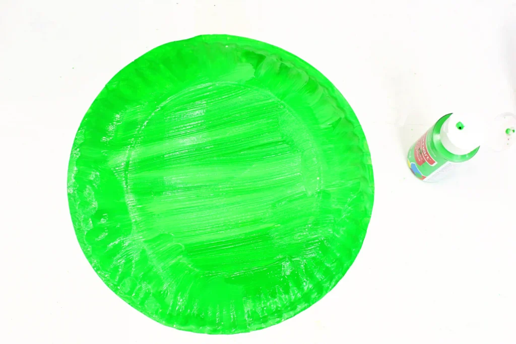 Bright neon green plate painted on a white surface with a green paint tube nearby, hinting at an art project.