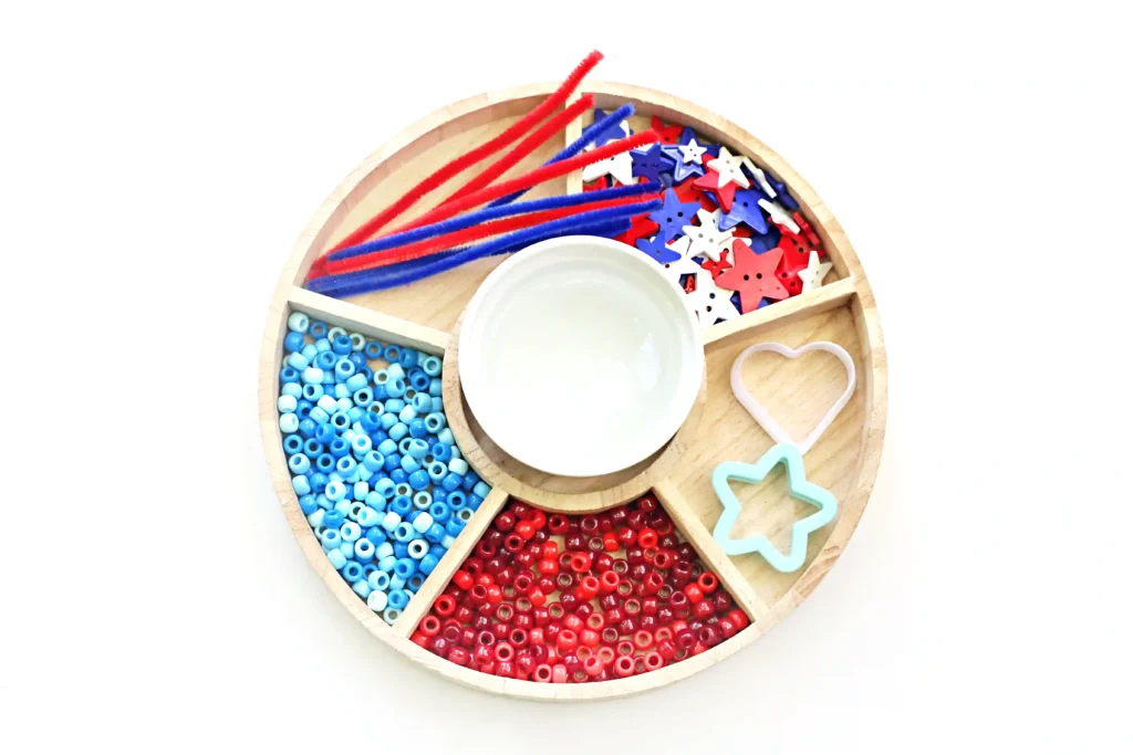 a tray with red, white, and blue buttons, red and blue pipe cleaners, bubble liquid, and red and blue pony beads