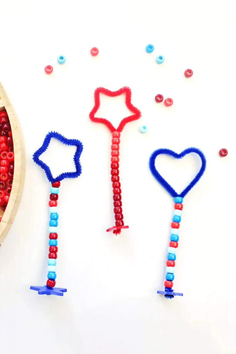 Beaded wands with red and blue pipe-cleaner shapes (star and heart) hanging from striped bead strings, with a wooden tray of beads visible on the left.