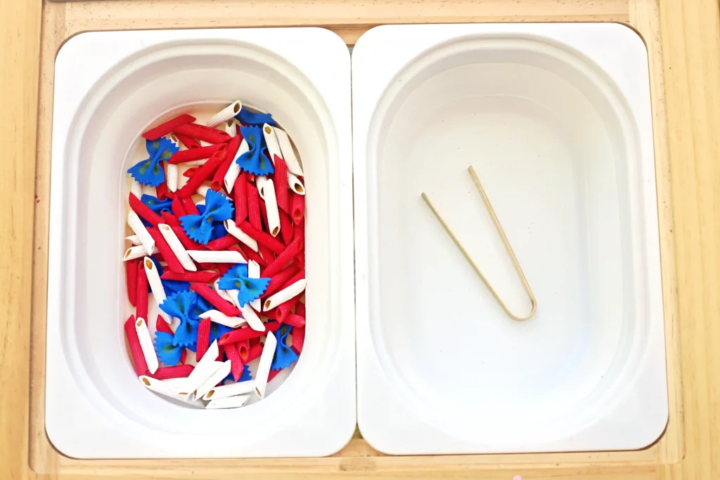 Left bowl overflowing with red, white, and blue pasta shapes (tube and flower shapes); right bowl empty with two wooden chopsticks resting inside.
