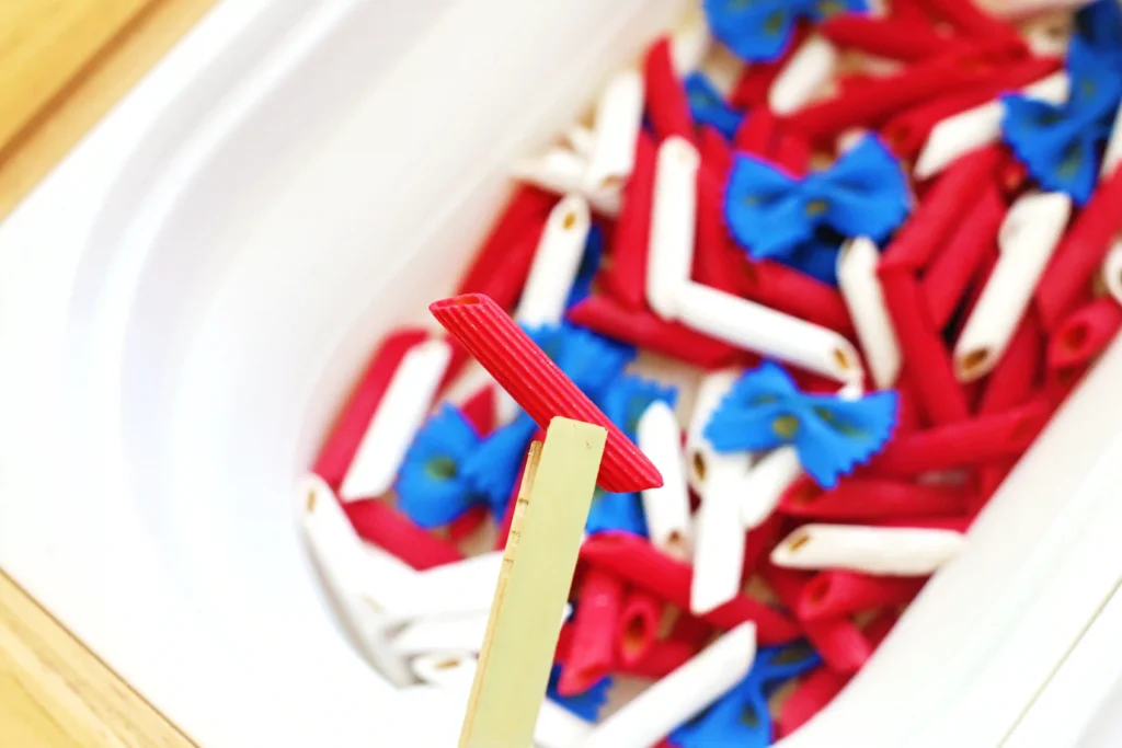 tongs picking up pasta dyed red, white and blue