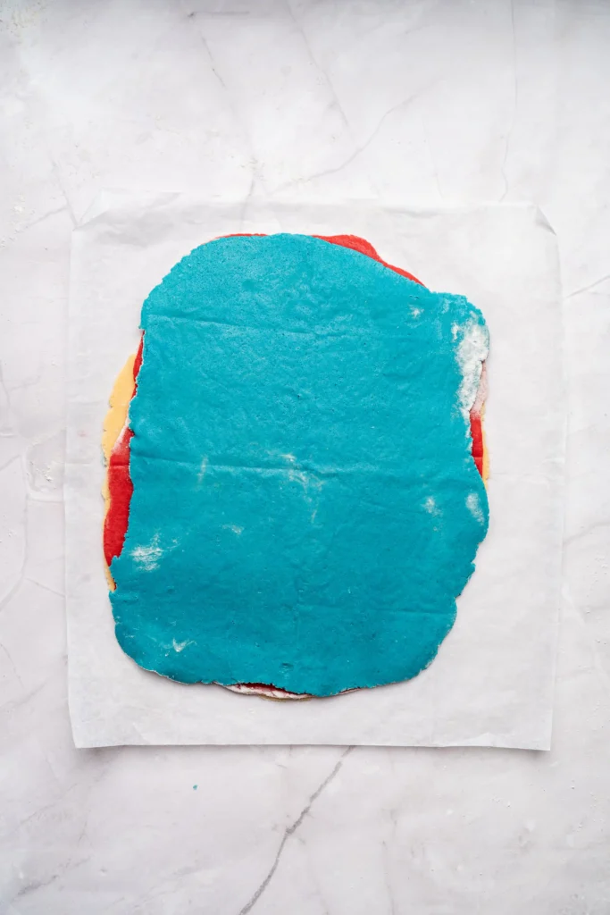 Top-down view of a layers of colored cookie dough placed on parchment on a marble surface.