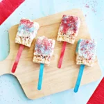 patriotic rice krispie treats on red and blue stick with melted white chocolate on top and red and blue sprinkles