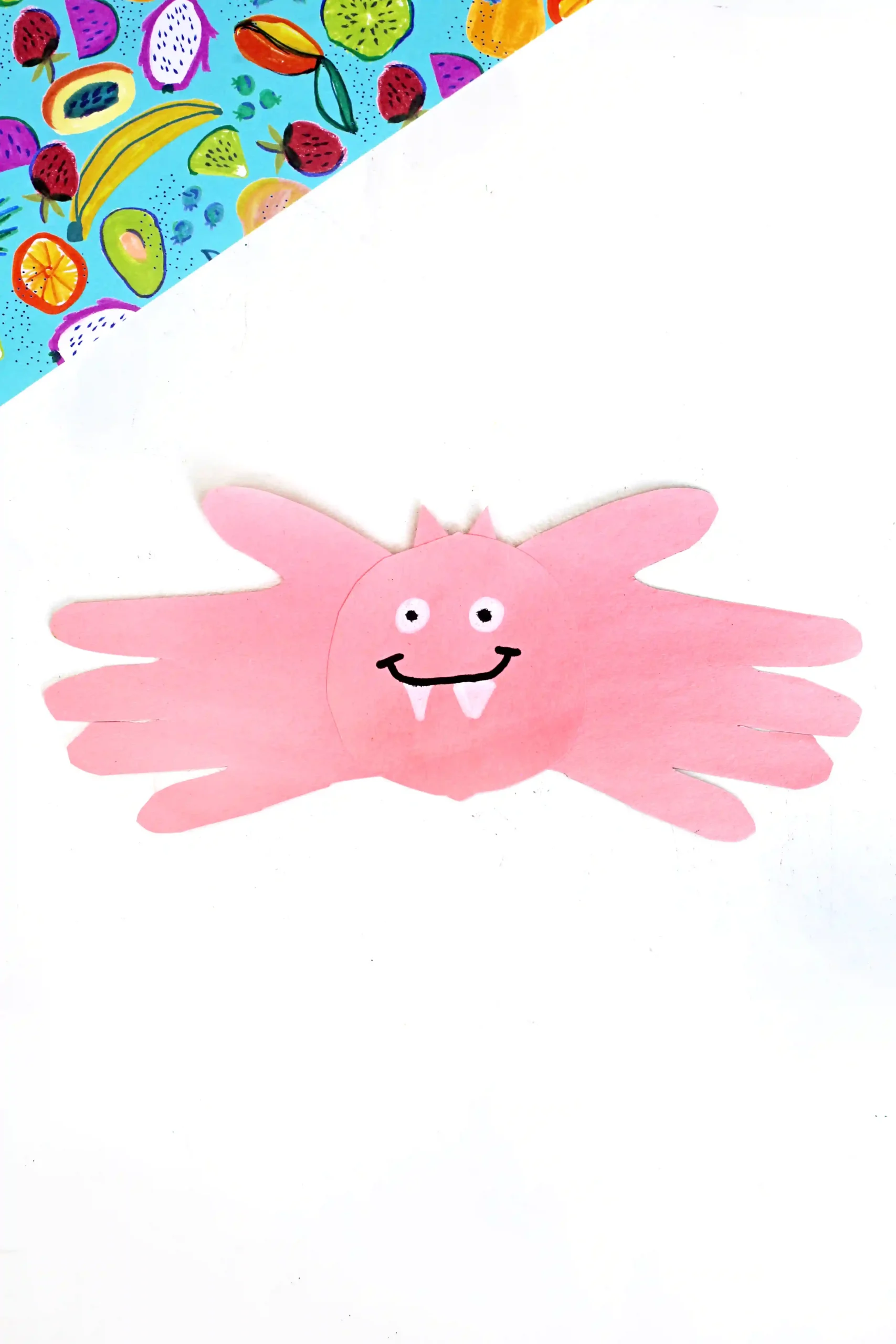 a pink bat handprint craft made out of pink construction paper with a drawn on face