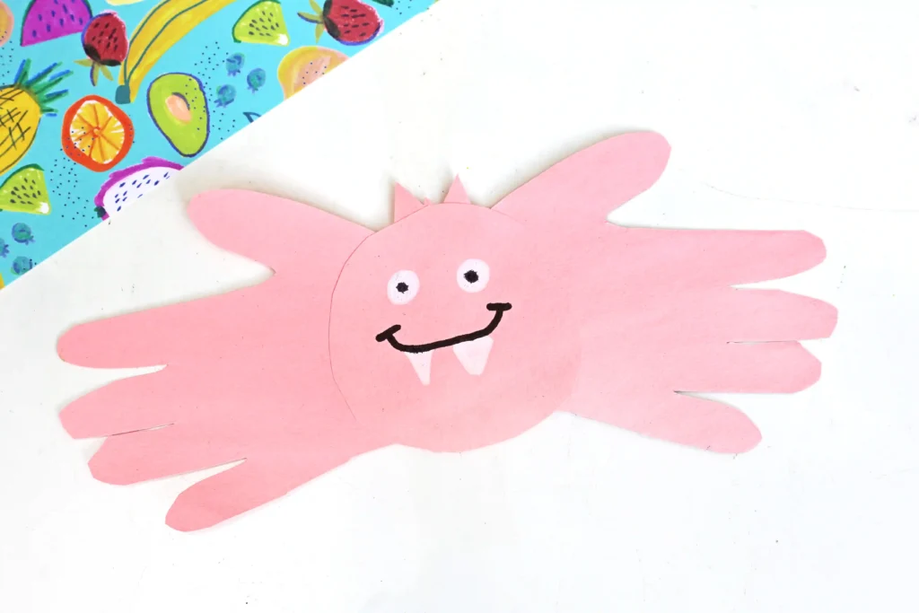a pink bat handprint craft made out of pink construction paper with a drawn on face