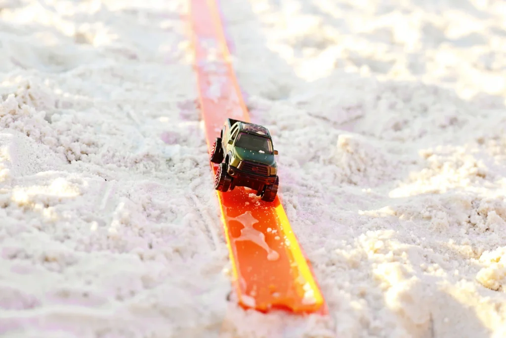 Green toy SUV racing down an orange plastic track across snowy ground.