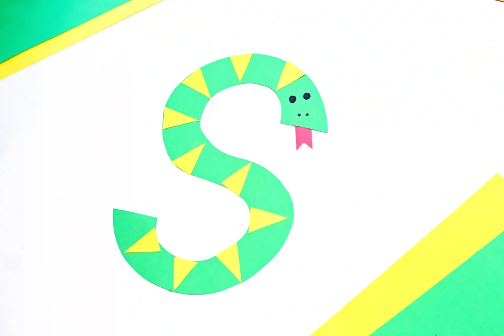 a letter s craft of a green S cut out of construction paper decorated to look like a snake with yellow scales and a red tongue that is perfect for a reptile lesson plan or reptile unit for preschool