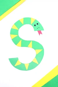 a letter s craft of a green S cut out of construction paper decorated to look like a snake with yellow scales and a red tongue