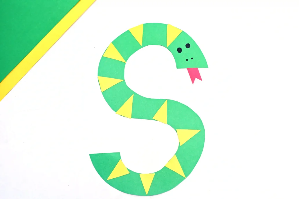 a letter craft for preschoolers of a green S cut out of construction paper decorated to look like a snake with yellow scales and a red tongue