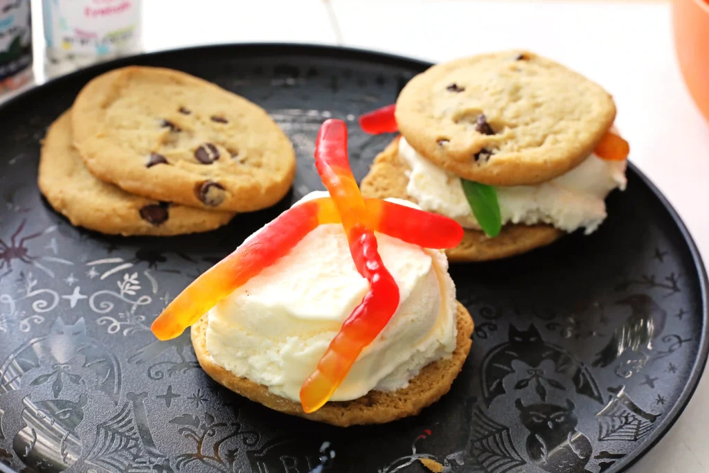 Plate with two chocolate chip cookies and open-faced mini sandwiches topped with vanilla ice cream and red/orange gummy worms for this Halloween Dessert