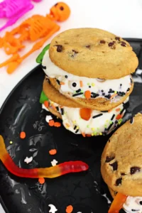 spooky ice cream sandwiches made with chocolate chip cookies, vanilla ice cream, gummy worms, and halloween sprinkles