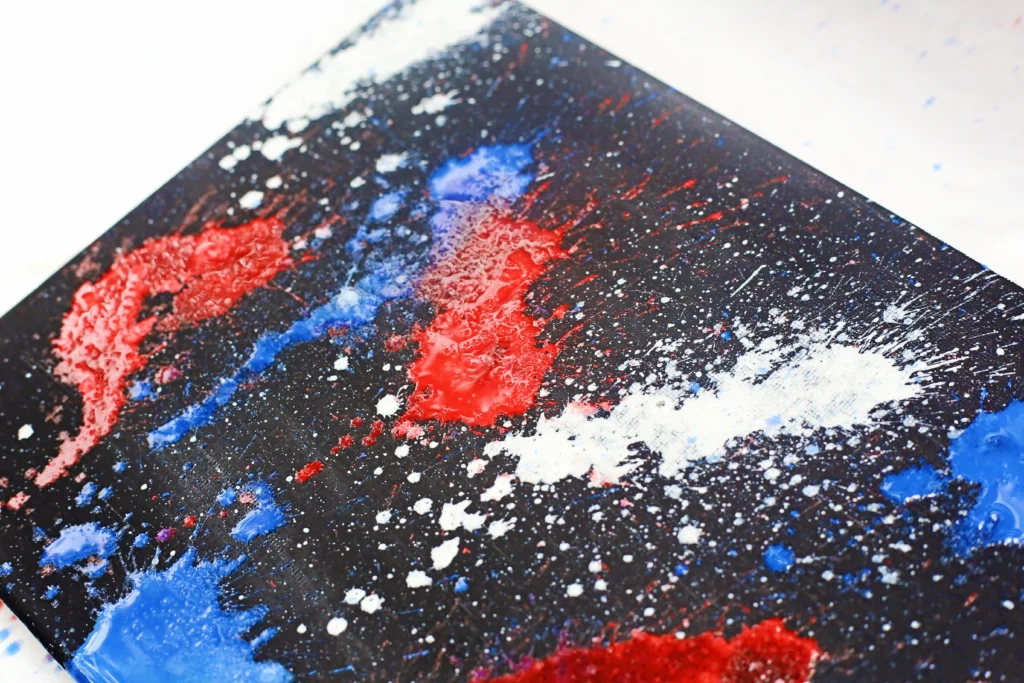 Close-up of an abstract painting with red, blue, and white paint splatters on a dark surface