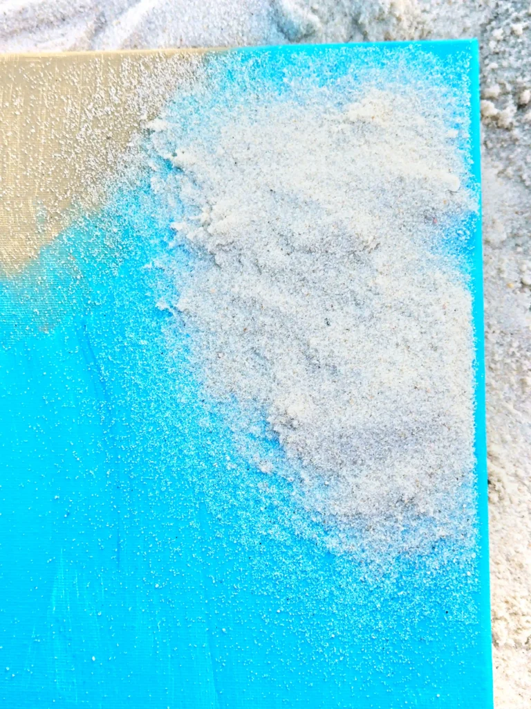 Close-up of a bright blue panel dusted with white powdery sand, with more sand scattered around it.