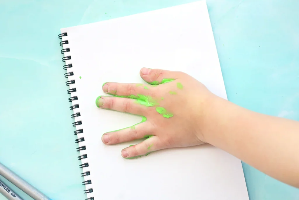 a kid stamping down their hand painted green on a piece of paper for this letter a craft