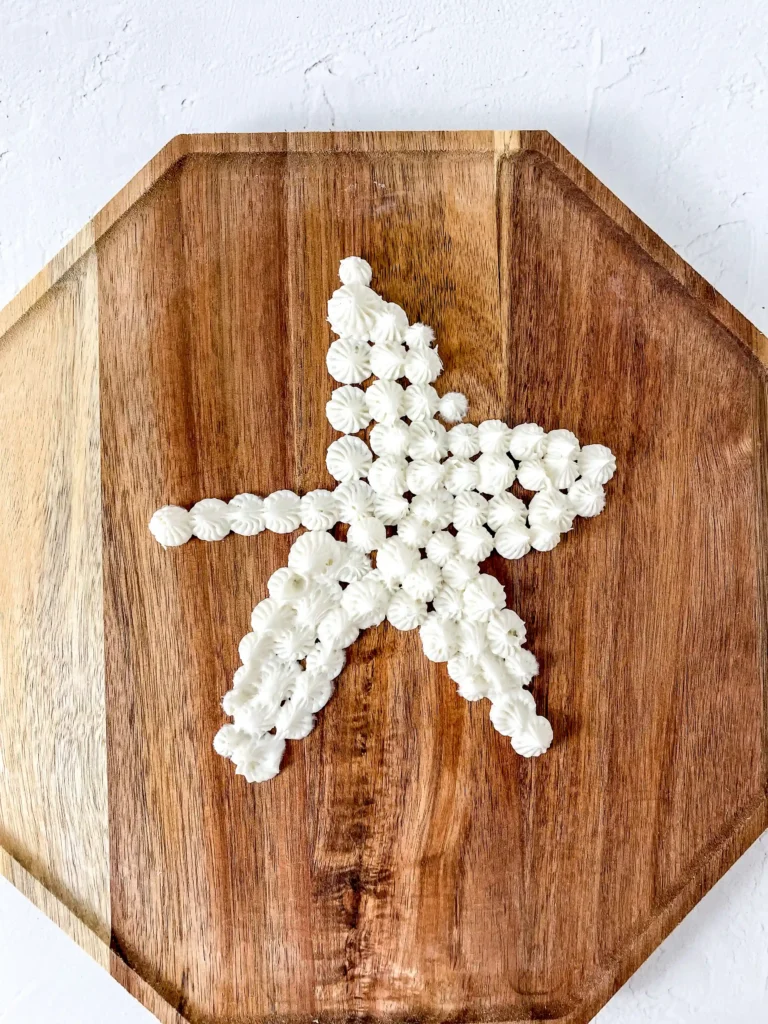 white dollops of buttercream in a star  shape on a wooden cutting board.