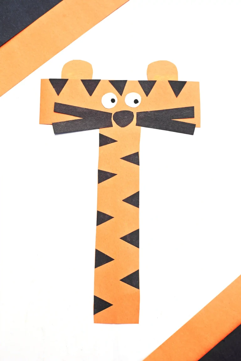 Orange paper tiger craft composed of strip-cut shapes with black triangular stripes, round white eyes, and a black nose to make up this letter activity